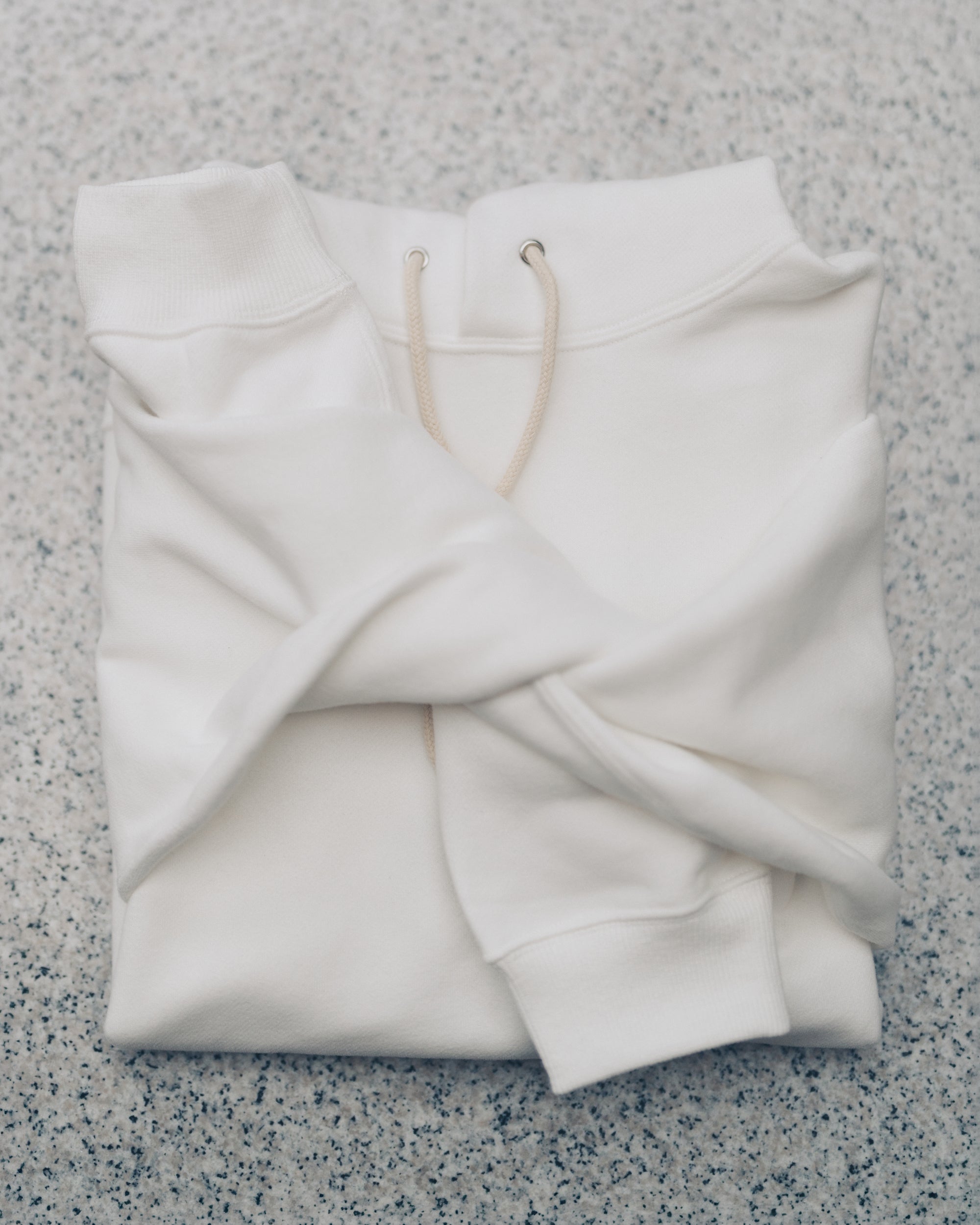 Aki Hoodie in White, folded on a granite surface