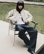 Model seated in a chrome chair wearing the Jiji Pant in Black with the Marilyn Bomber in Sage